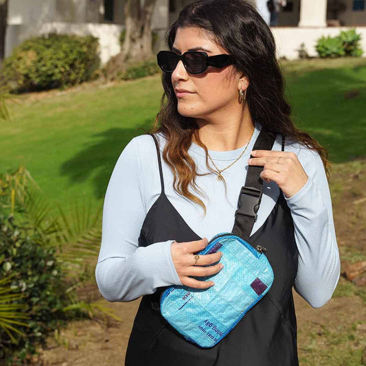 Woman holding a blue bag outdoors with greenery in the background