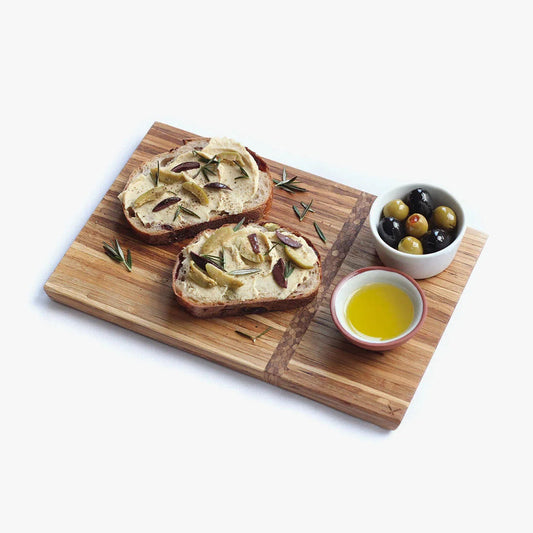 Two slices of bread with olive tapenade on a wooden board with a bowl of olives and oil.